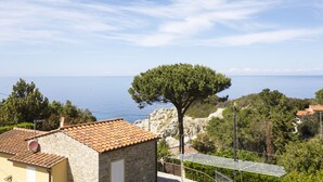 A stone building with a tiled roof, a large tree, and a view of the sea. - Appartamenti Cotoncello (Marciana)
