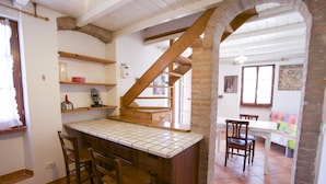 A kitchen with a tiled countertop, wooden chairs, and a brick wall. - Villa Gloria (Portoferraio)