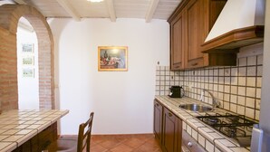 A kitchen with a tiled backsplash, wooden cabinets, a gas stove, and a sink. - Villa Gloria (Portoferraio)