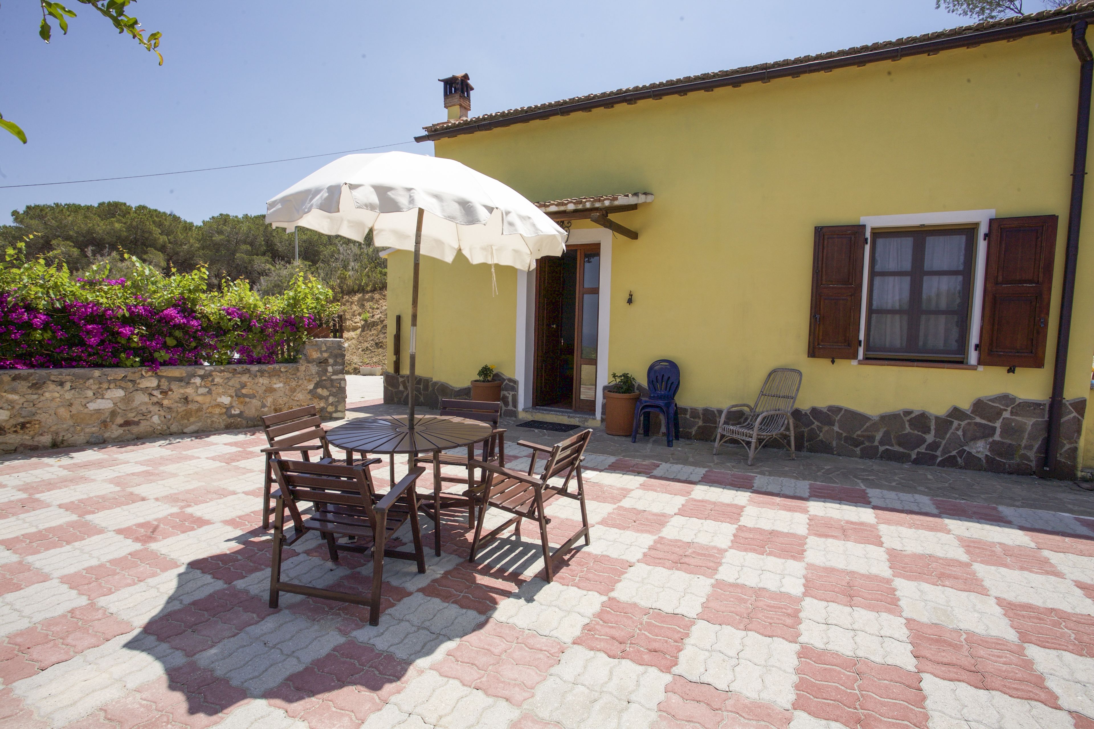A yellow building with a tiled patio, wooden furniture, and a white umbrella.