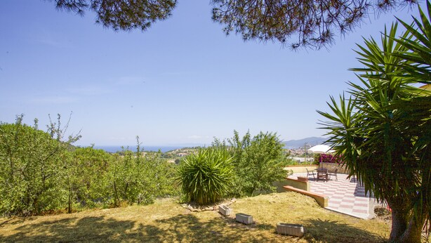 A patio area with a checkered floor, surrounded by greenery and a view of distant hills. - Villa Gloria (Portoferraio)