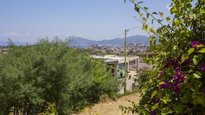 A view of a coastal area with a modern building, dense greenery, and mountains in the background. - Villa Gloria (Portoferraio)