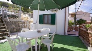 A patio with a white table and chairs, a green umbrella, and a stone wall. - Appartamento Le Conchiglie (Portoferraio)