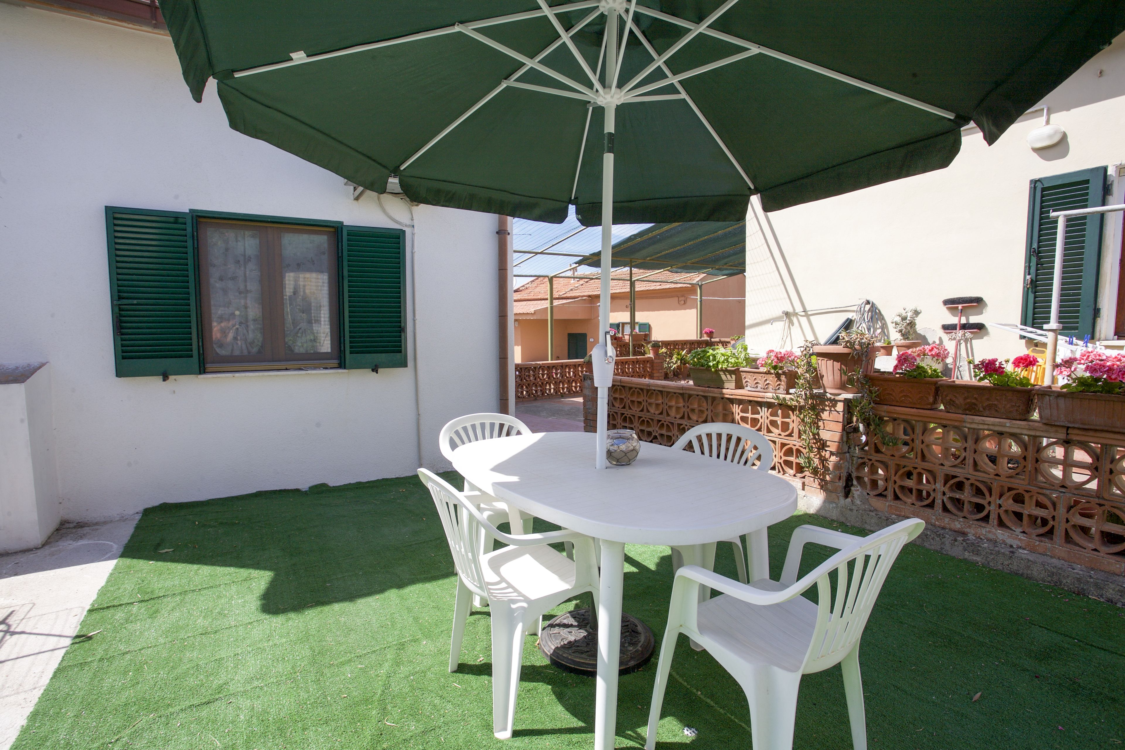 A patio with a white table and chairs, a green umbrella, and a decorative fence with potted plants.