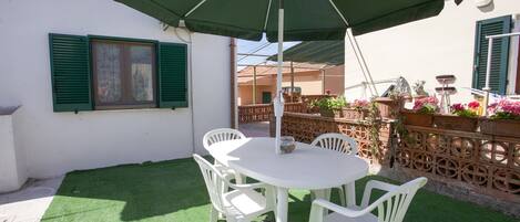 A patio with a white table and chairs, a green umbrella, and a decorative fence with potted plants.