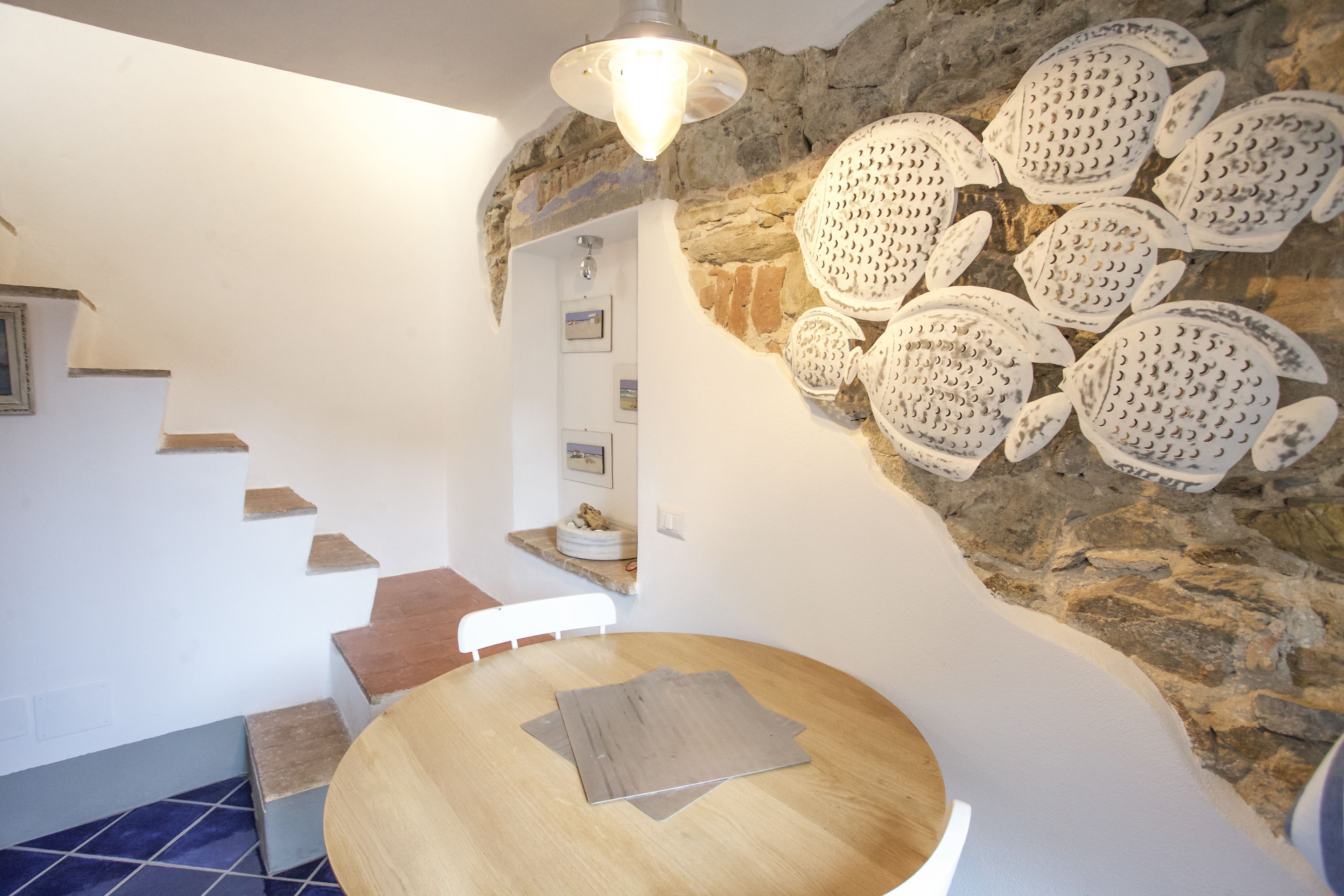 Una escalera lleva a un dormitorio con pared de piedra y una mesa redonda de madera.
