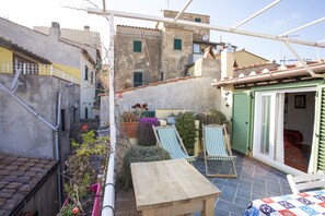 A courtyard with a wooden table, two striped lounge chairs, and potted plants. - Appartamento Tetti Storici (Capoliveri)