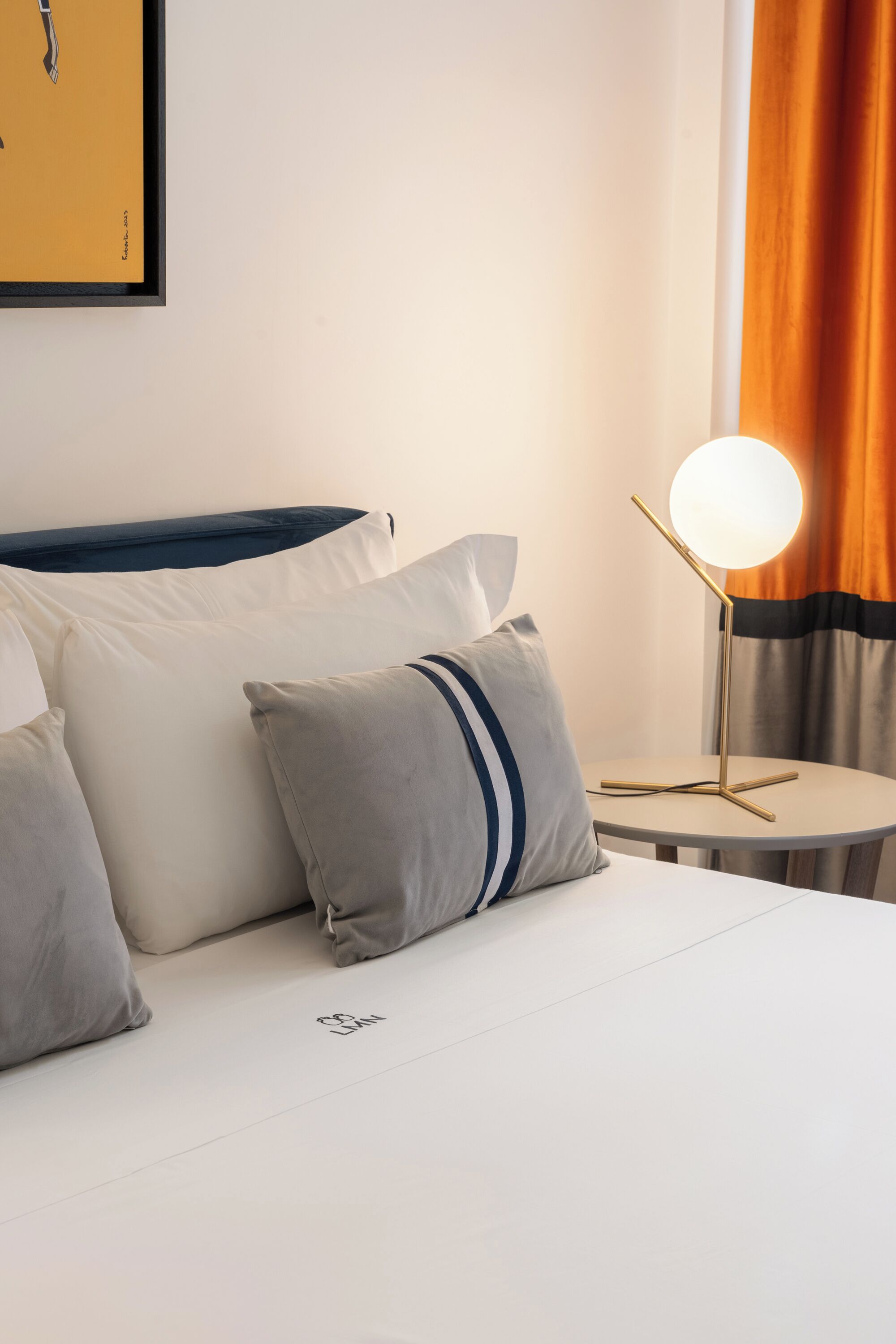A hotel room with a neatly made bed, a bedside table with a lamp, and a framed picture on the wall.