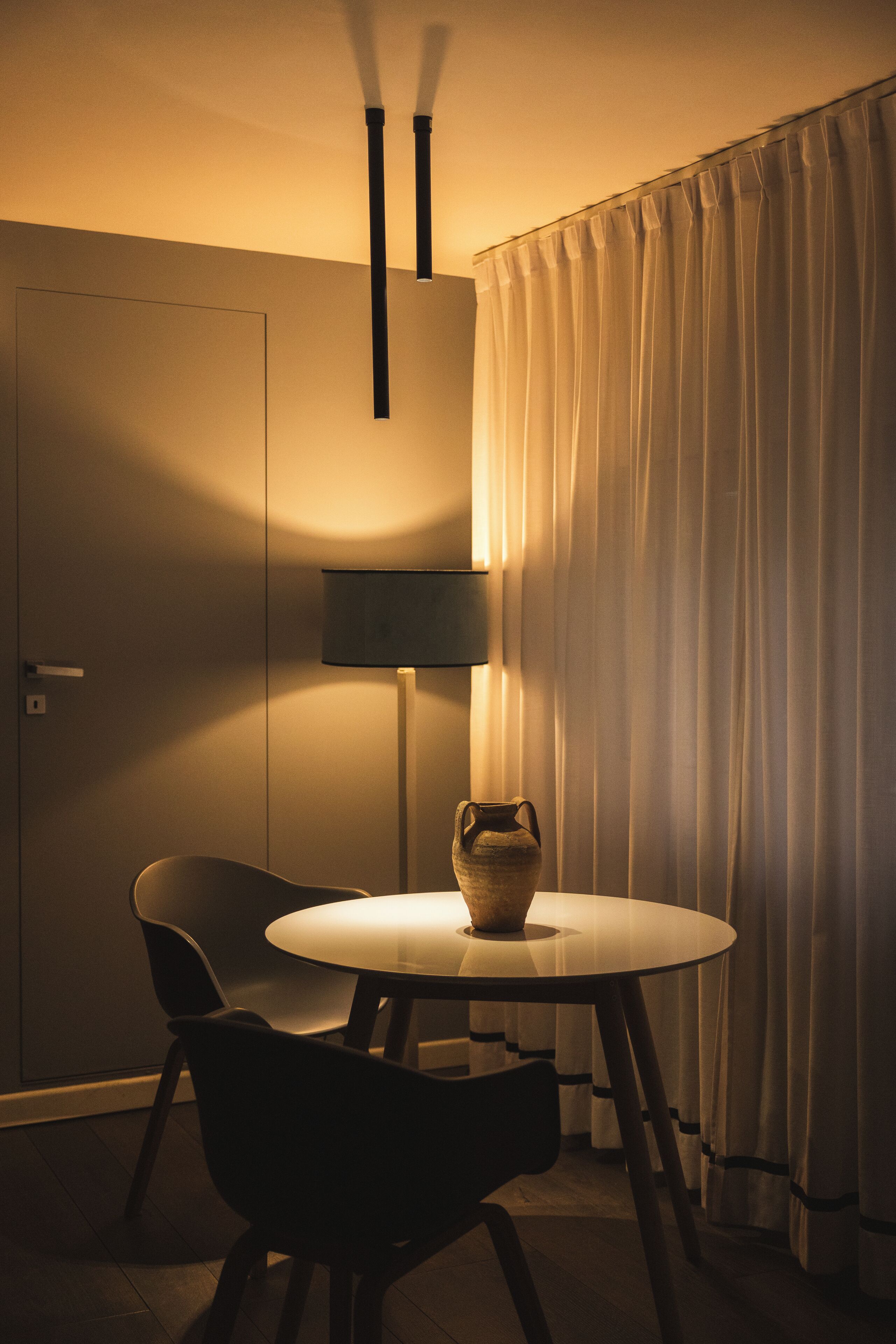 Una habitación con una mesa redonda, una silla, una lámpara y una cortina.
