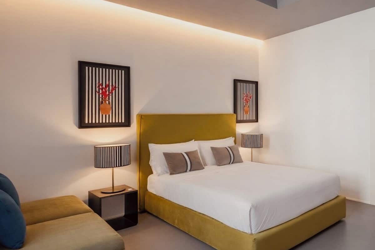A modern bedroom with a large bed, two bedside tables with lamps, and two wall-mounted artworks.