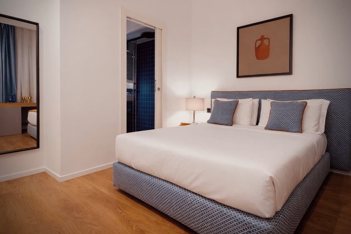 A neatly arranged hotel room with a large bed, a bedside table with a lamp, and a framed picture on the wall.