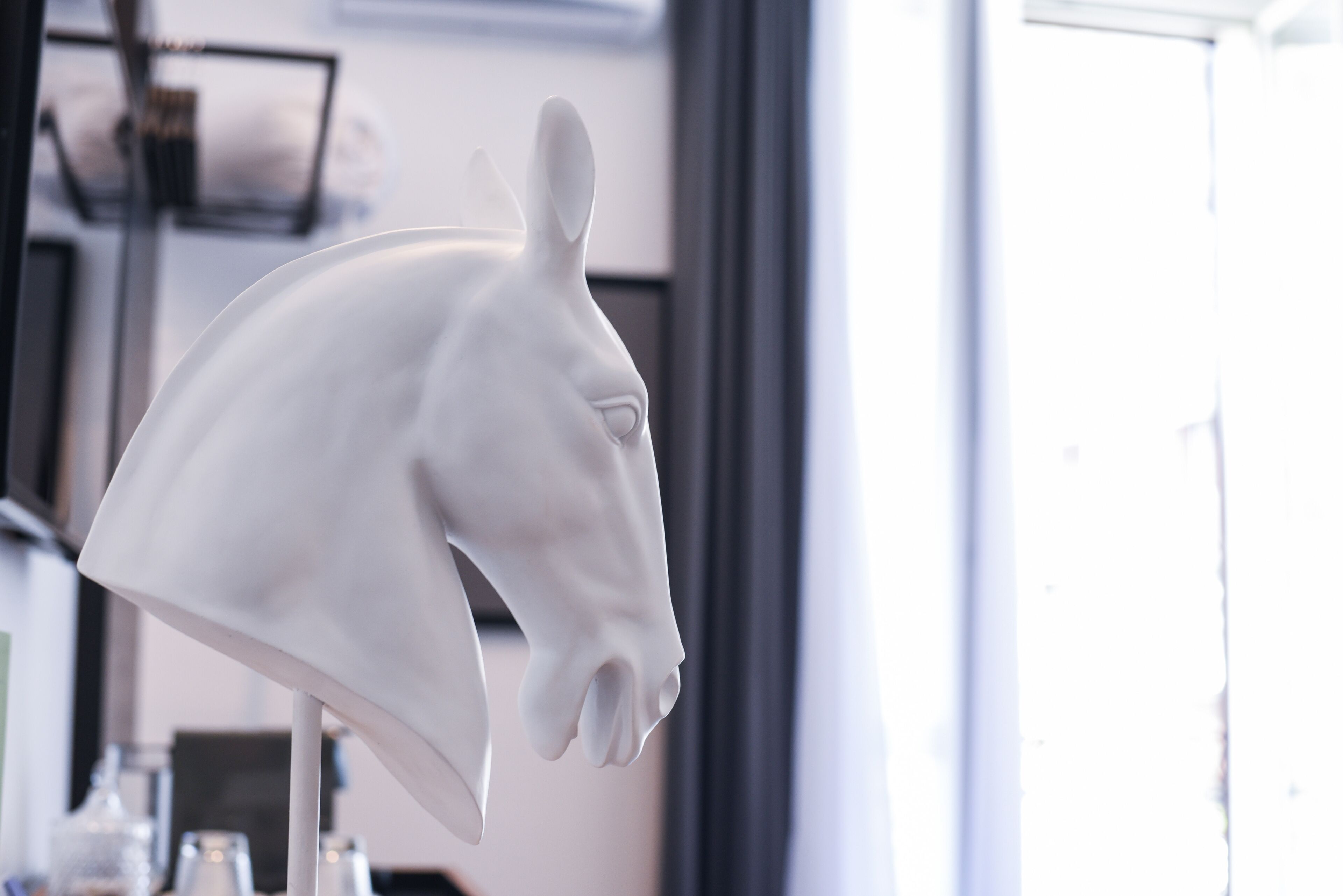 Een witte paardenbeeld in een goed verlichte kamer, met een raam en planken op de achtergrond.
