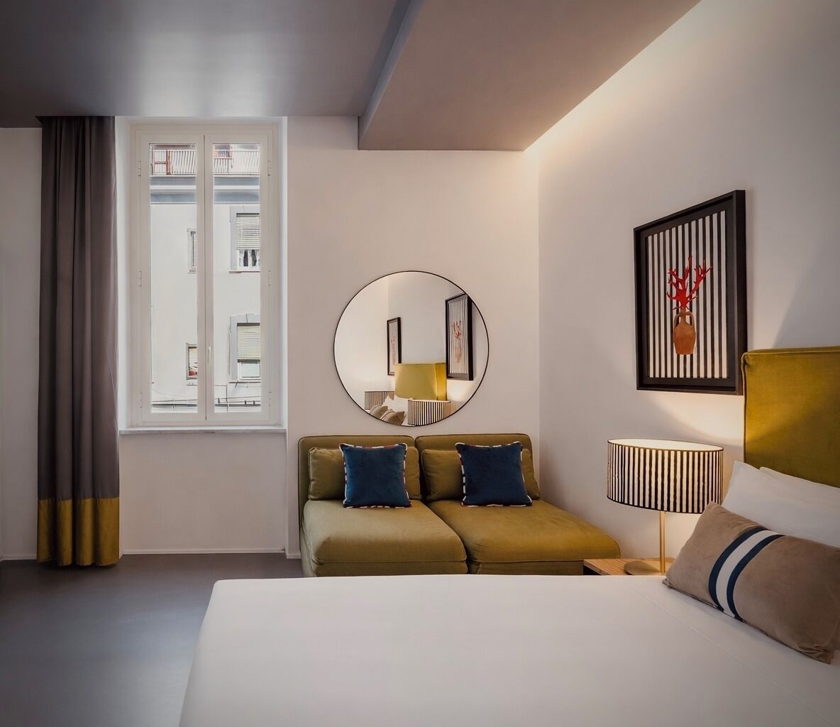 Ein modernes Hotelzimmer mit Bett, einer Couch, einem runden Spiegel, einer Lampe und einem gerahmten Kunstwerk an der Wand.