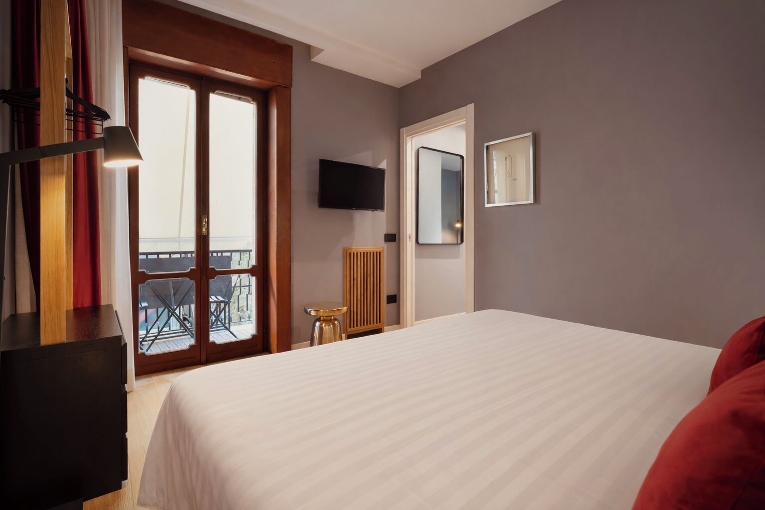 Een hotelkamer met een groot bed, een aan de muur bevestigde televisie, een tafeltje en een balkon met uitzicht.