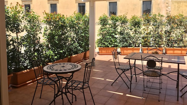 Un patio coperto con pavimento piastrellato, sedute da esterno e piante in vaso.
