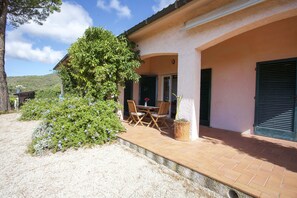 A house with a patio, a dining table with chairs, and a large tree. - Villino Lacona (Capoliveri)