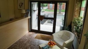 A lobby with a reception desk, a white armchair, a coffee table with a fruit bowl, and a door leading outside. - Hotel Zum Grafen Hallermunt (Springe)