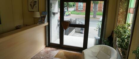 Un vestíbulo con mostrador de recepción, un sillón blanco, una mesa de centro con frutero, y una puerta que da al exterior.