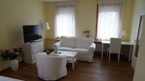 A hotel room with a white sofa, a small table, a TV, a desk, and a chair. - Hotel Zum Grafen Hallermunt (Springe)