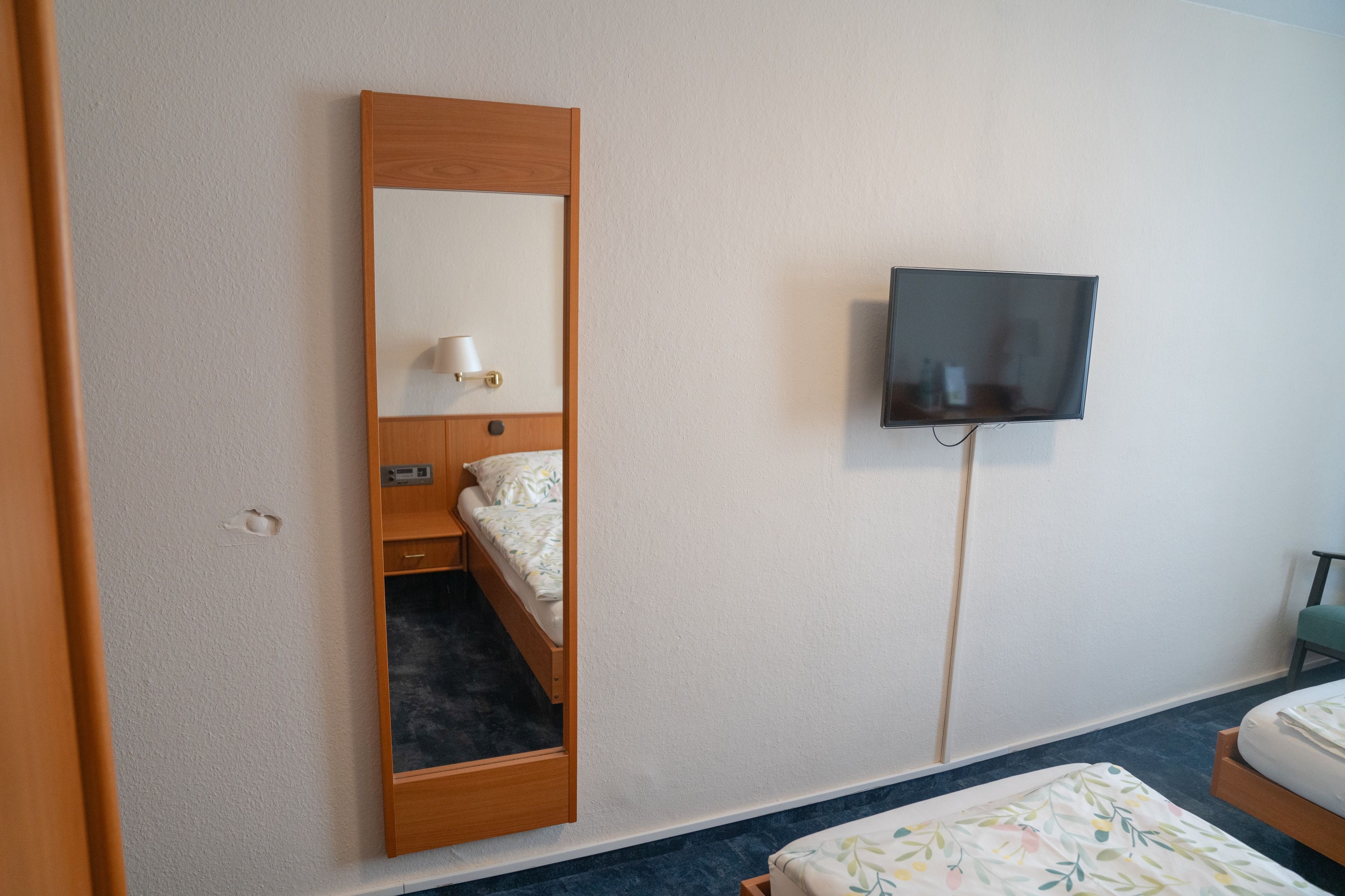 Una habitación de hotel con cama, televisor montado en la pared y un armario de madera.