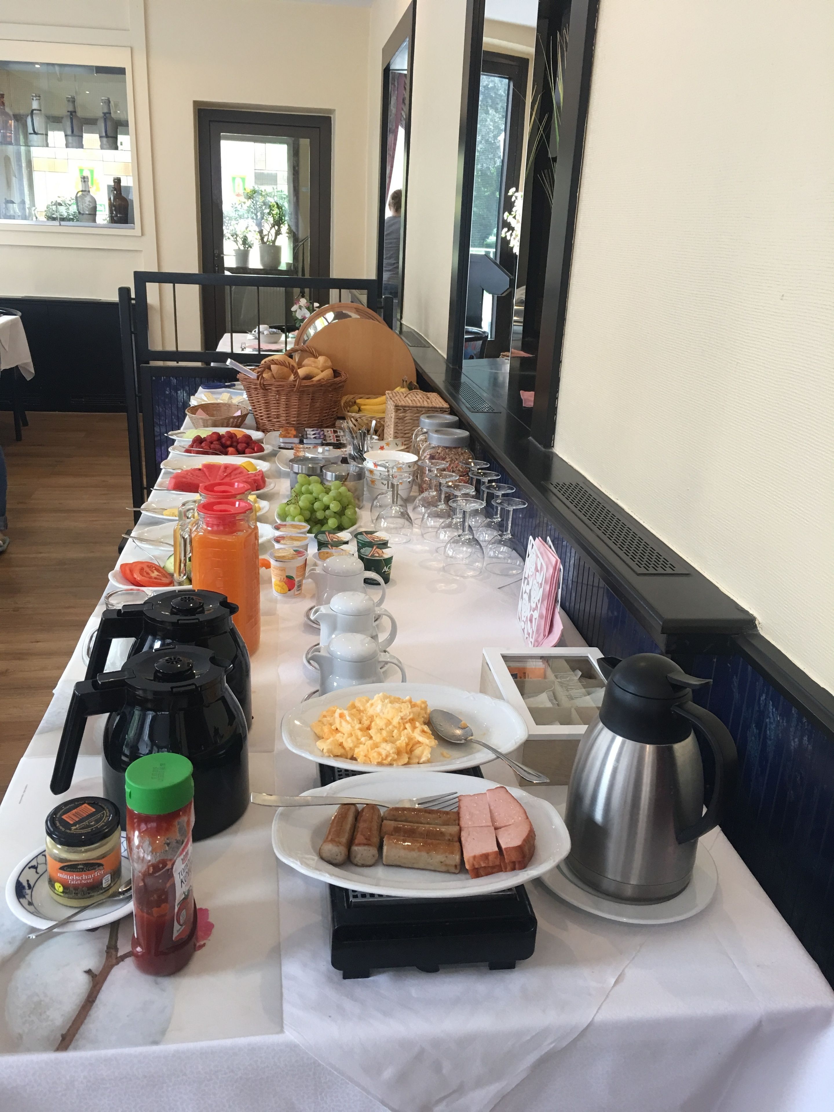 A buffet table with various food items, including fruits, bread, and condiments.