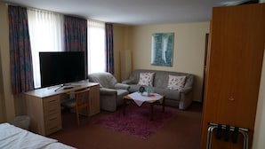 A hotel room with a bed, a desk with a TV, a sofa, and a small table with a vase. - Hotel Zum Grafen Hallermunt (Springe)