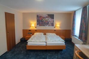 Une chambre d’hôtel avec un lit double, deux lampes de chevet, un tableau au mur et une fenêtre avec des rideaux.