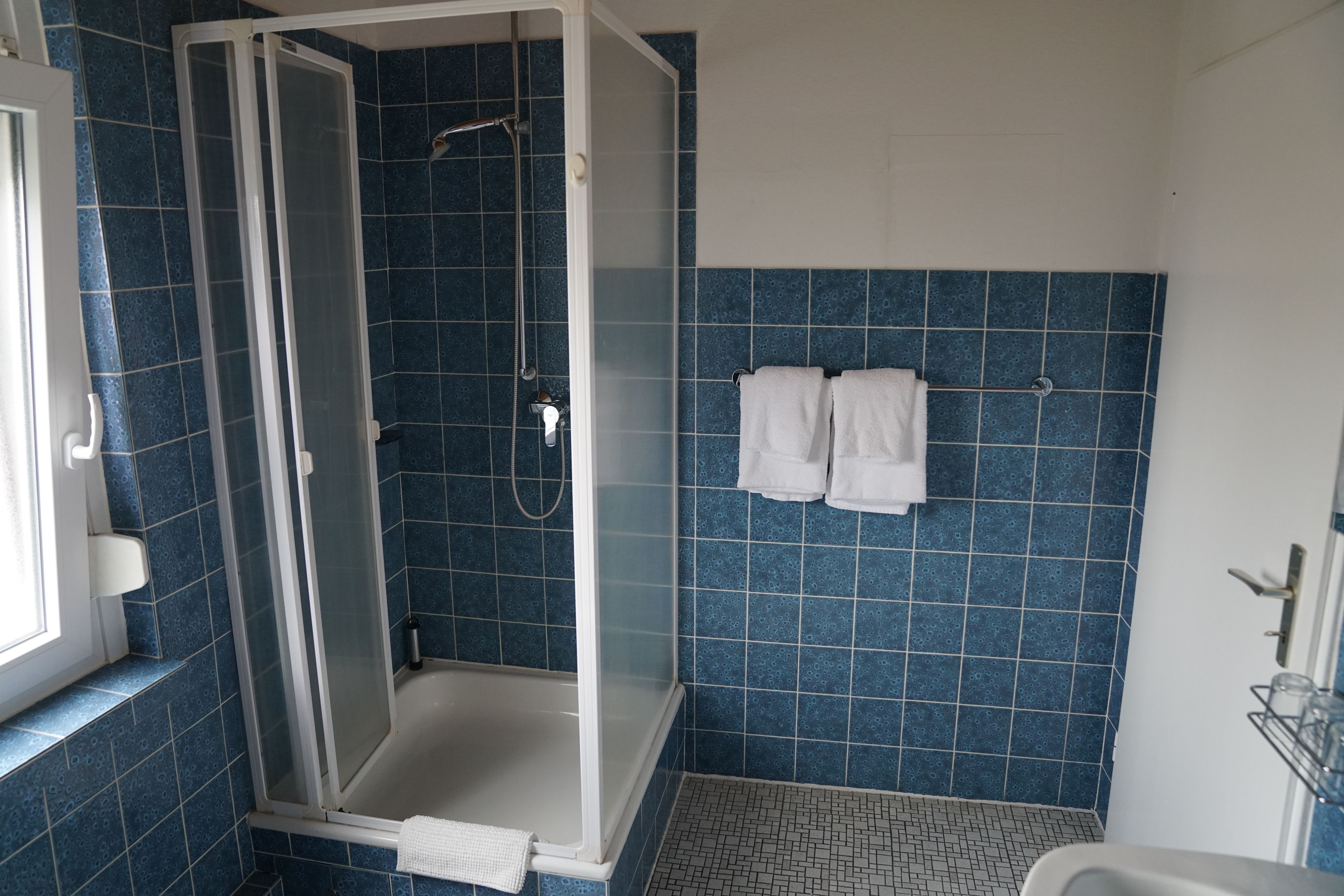 Un baño con ducha de vidrio, paredes con azulejos azules y un lavamanos blanco.