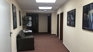 A hallway with a brown carpet, a black sofa, and framed artwork on the walls. - Hotel Zum Grafen Hallermunt (Springe)
