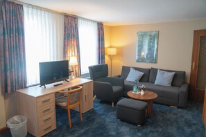 A hotel room with a desk, chair, sofa, ottoman, and a TV. - Hotel Zum Grafen Hallermunt (Springe)