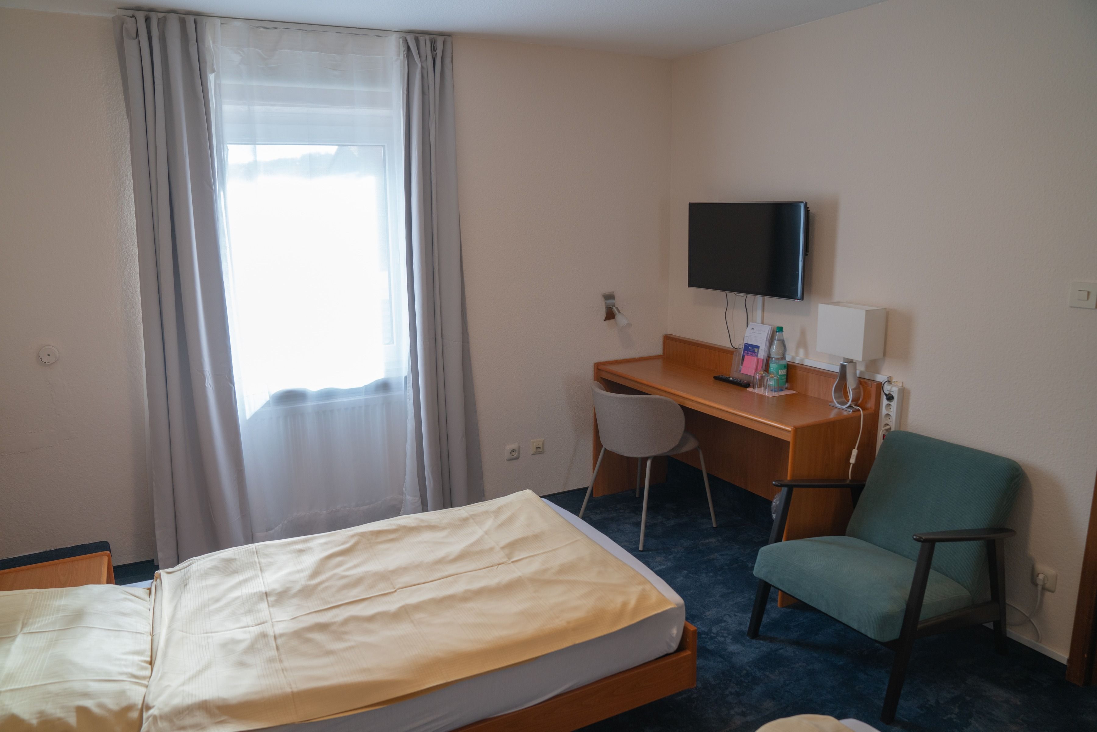 A hotel room with a bed, a desk, a chair, a television, and a window with curtains.