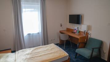 A hotel room with a bed, a desk, a chair, a television, and a window with curtains.