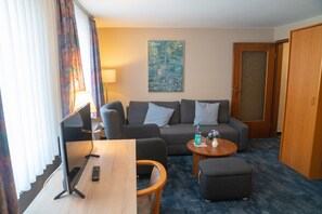 Une chambre d’hôtel comprenant un canapé, un bureau avec un ordinateur, une petite table ronde et une porte.