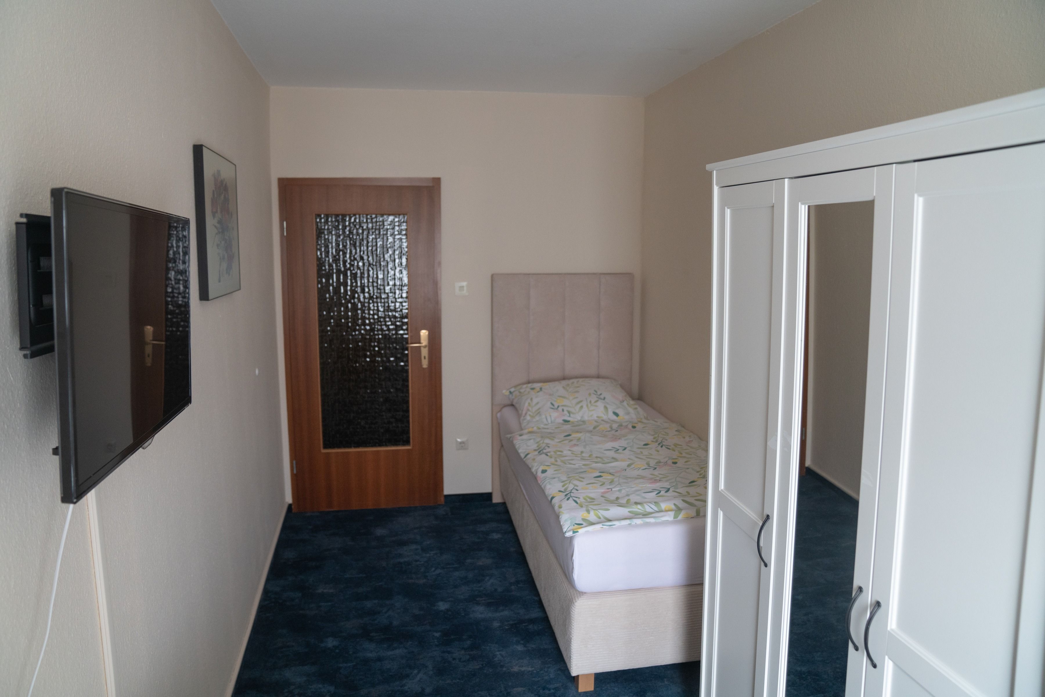 Un pasillo estrecho con una cama, un armario y una puerta con un panel de vidrio decorativo.