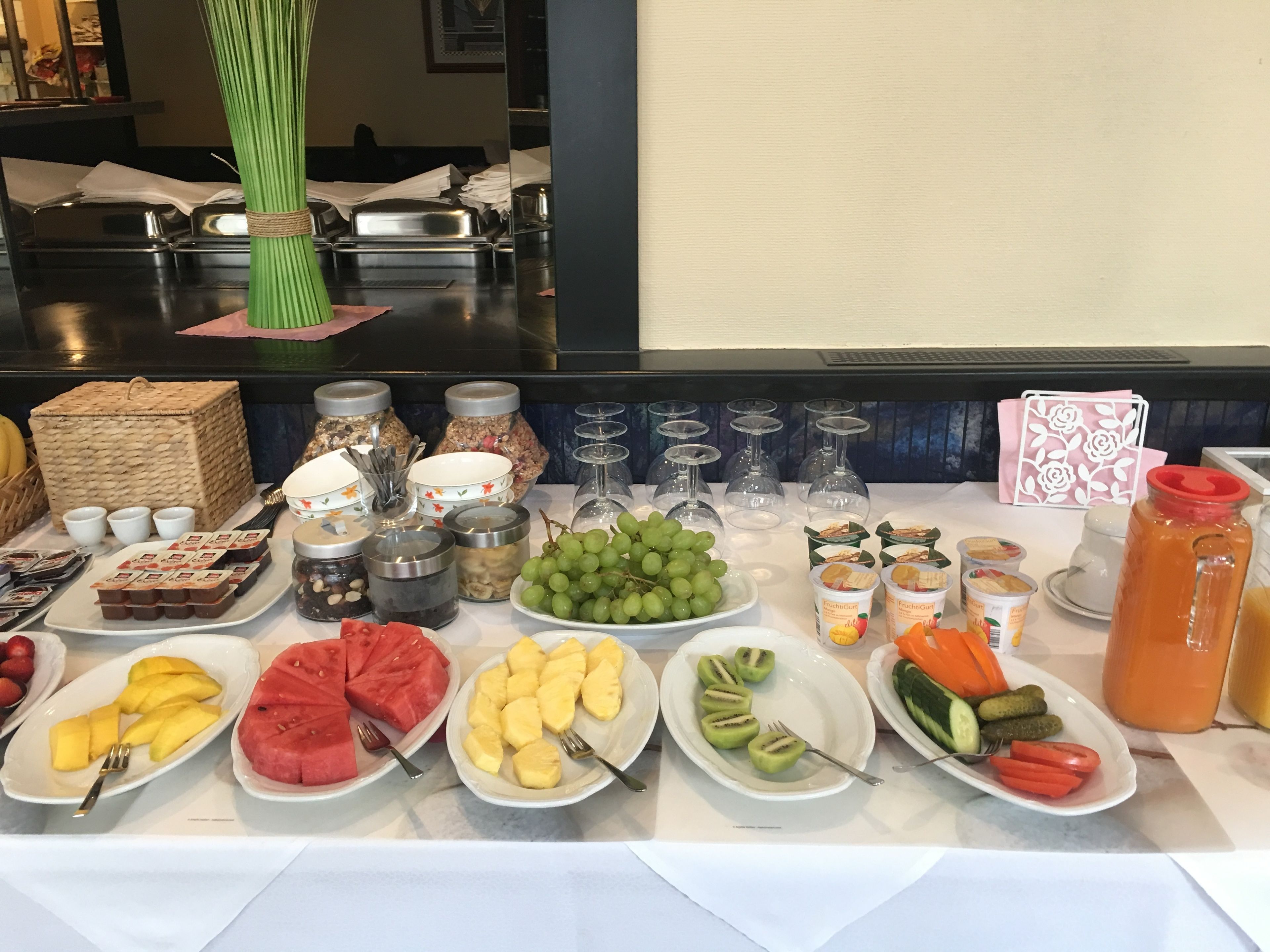 Uma mesa de buffet com diversas opções de comida, incluindo frutas, sobremesas e bebidas.