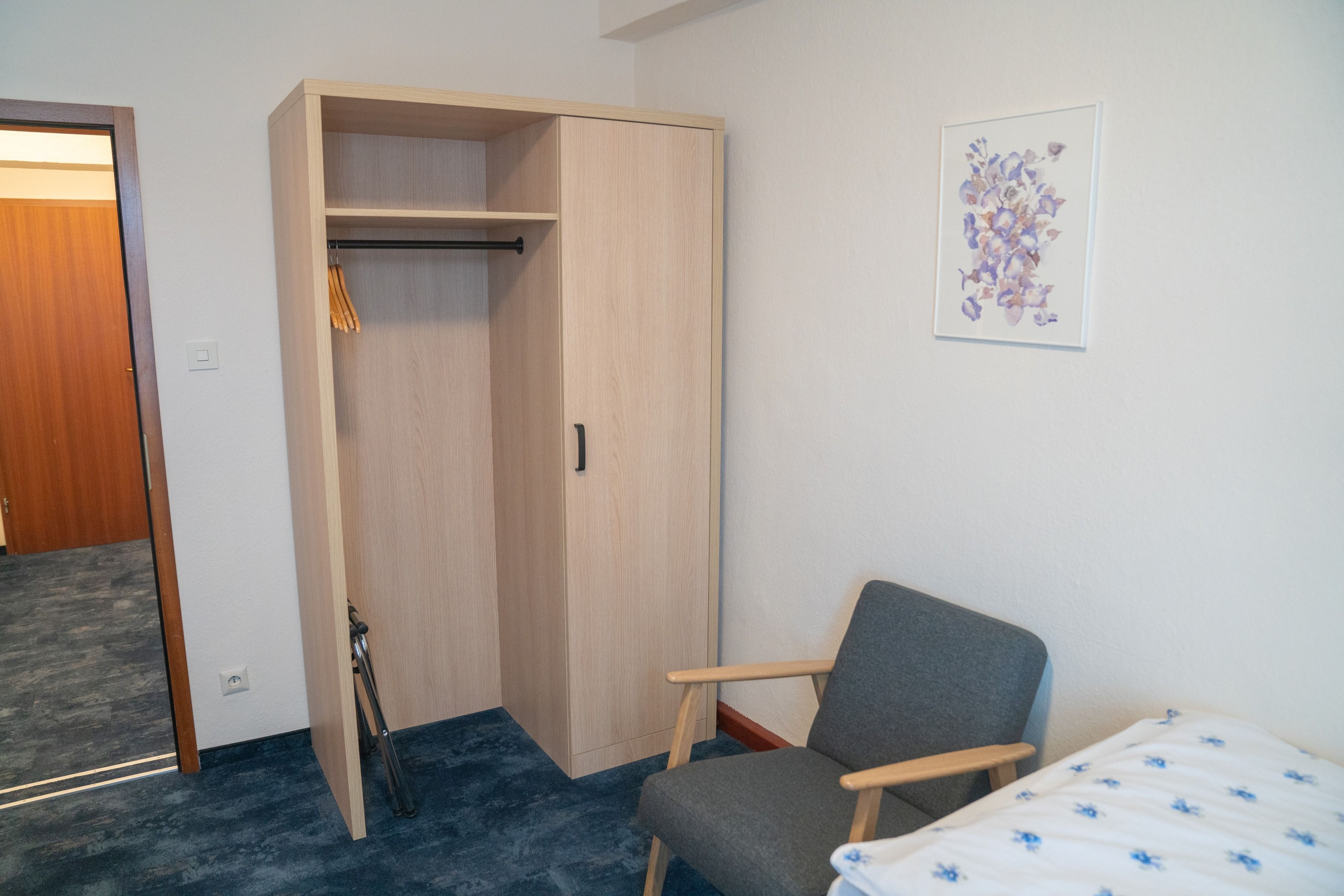 Una habitación con una cama individual, una silla, un armario y una puerta.