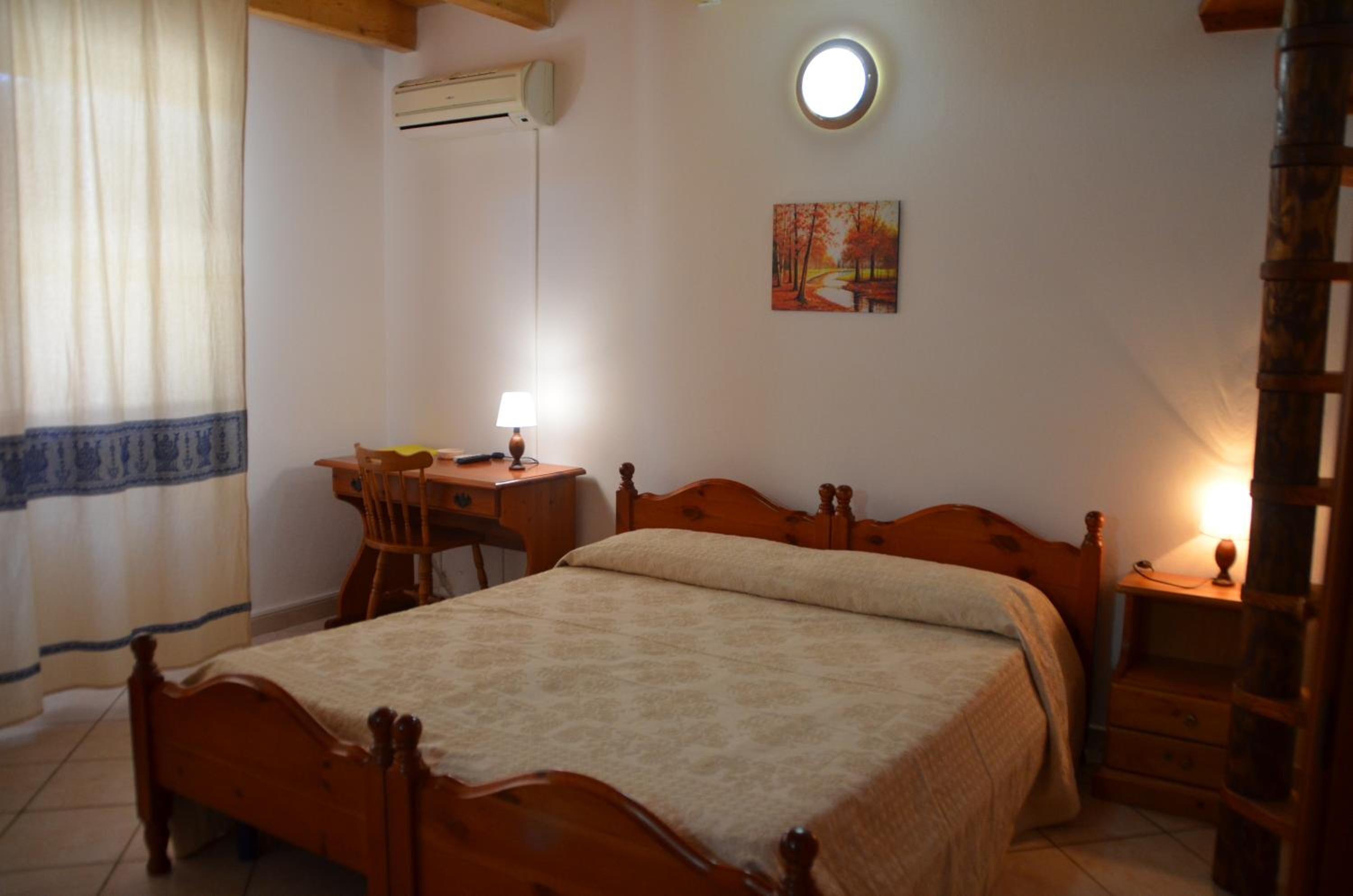 Un dormitorio con cama de madera, un escritorio con silla, una mesita de noche y un aire acondicionado instalado en la pared.