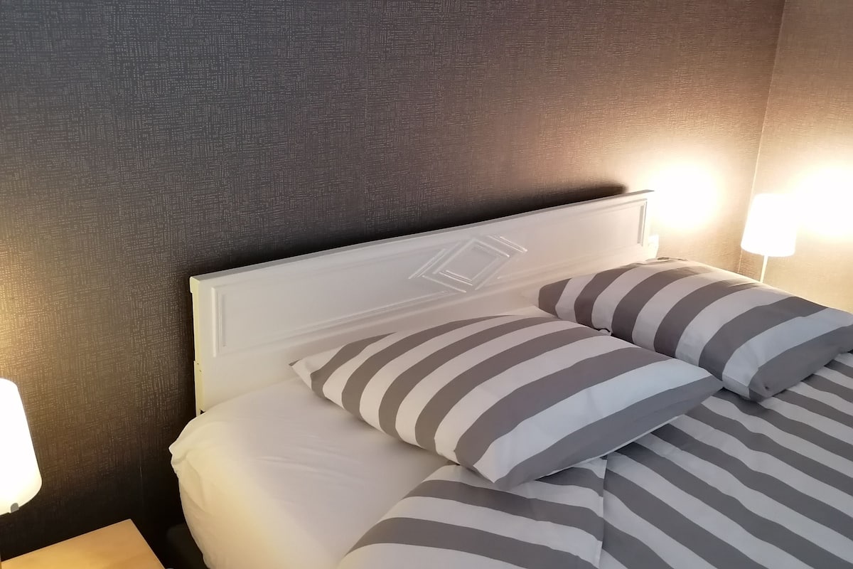 A neatly made bed with striped bedding, a bedside table with a lamp, and a textured wall.