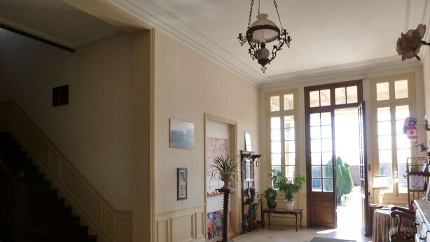 A spacious hallway with a staircase on the left, a large window on the right, and a chandelier hanging from the ceiling.