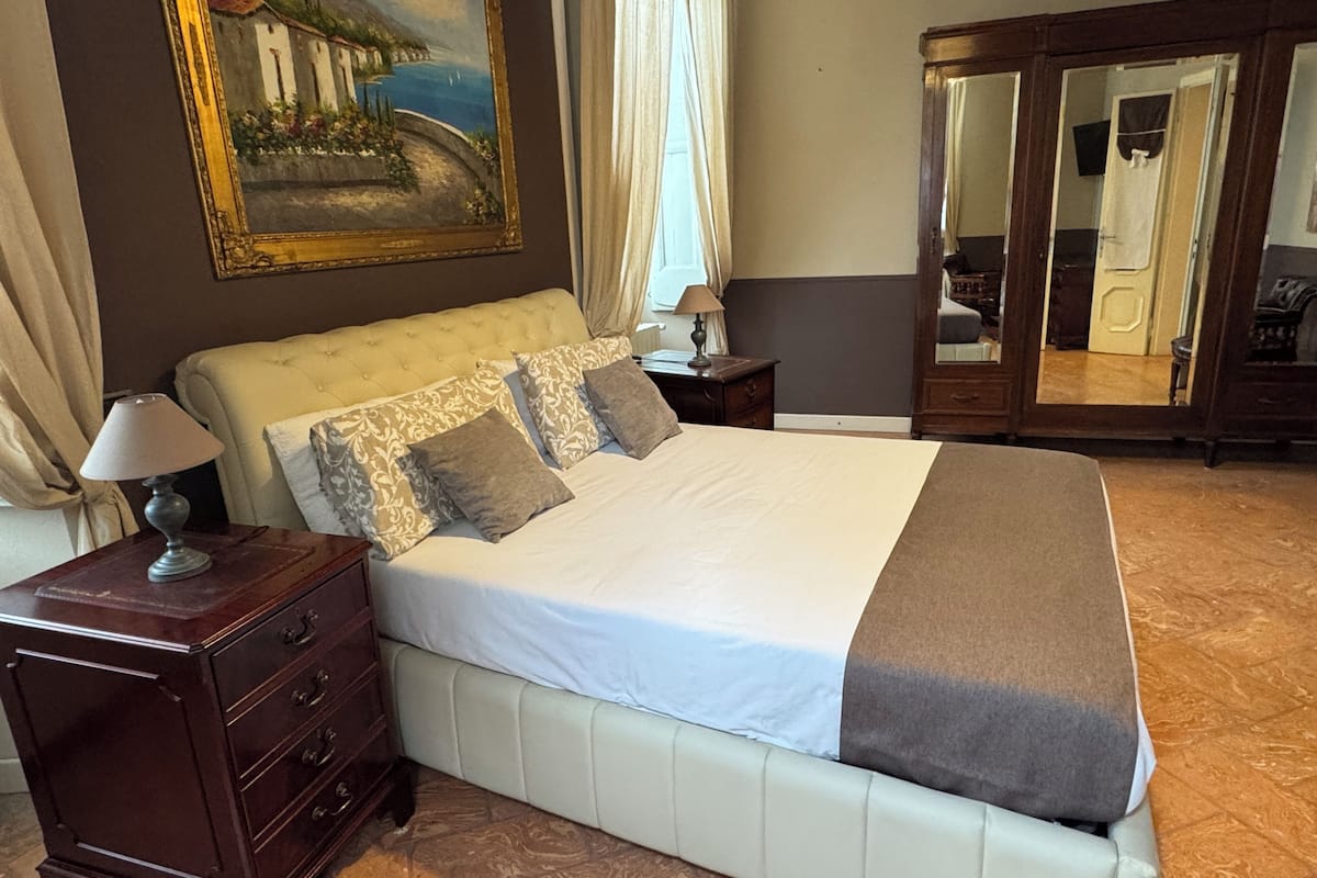 A bedroom with a bed, nightstand, dresser, and a painting on the wall.