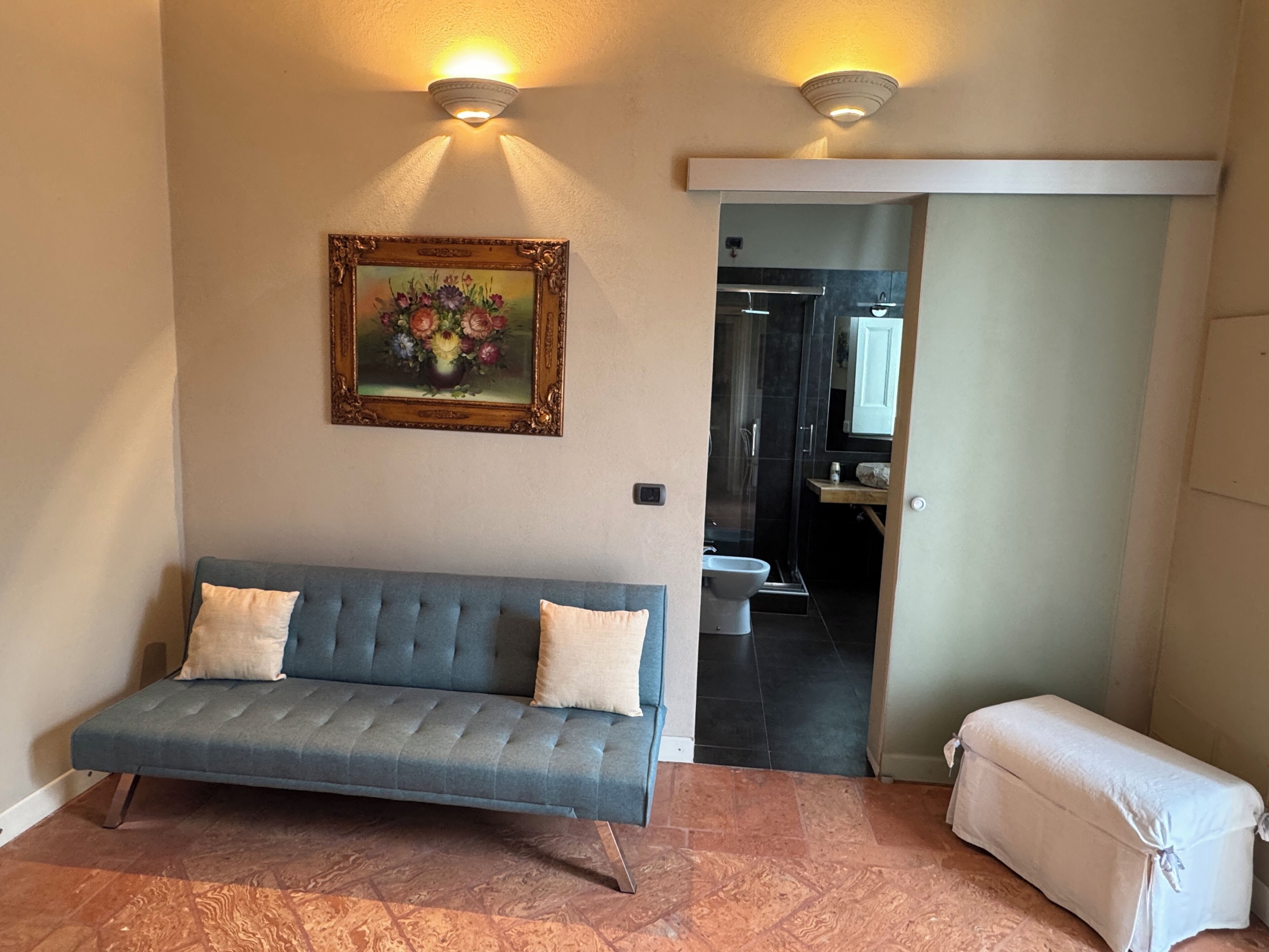 A room with a sofa, a painting, a bench, and a doorway leading to a bathroom.