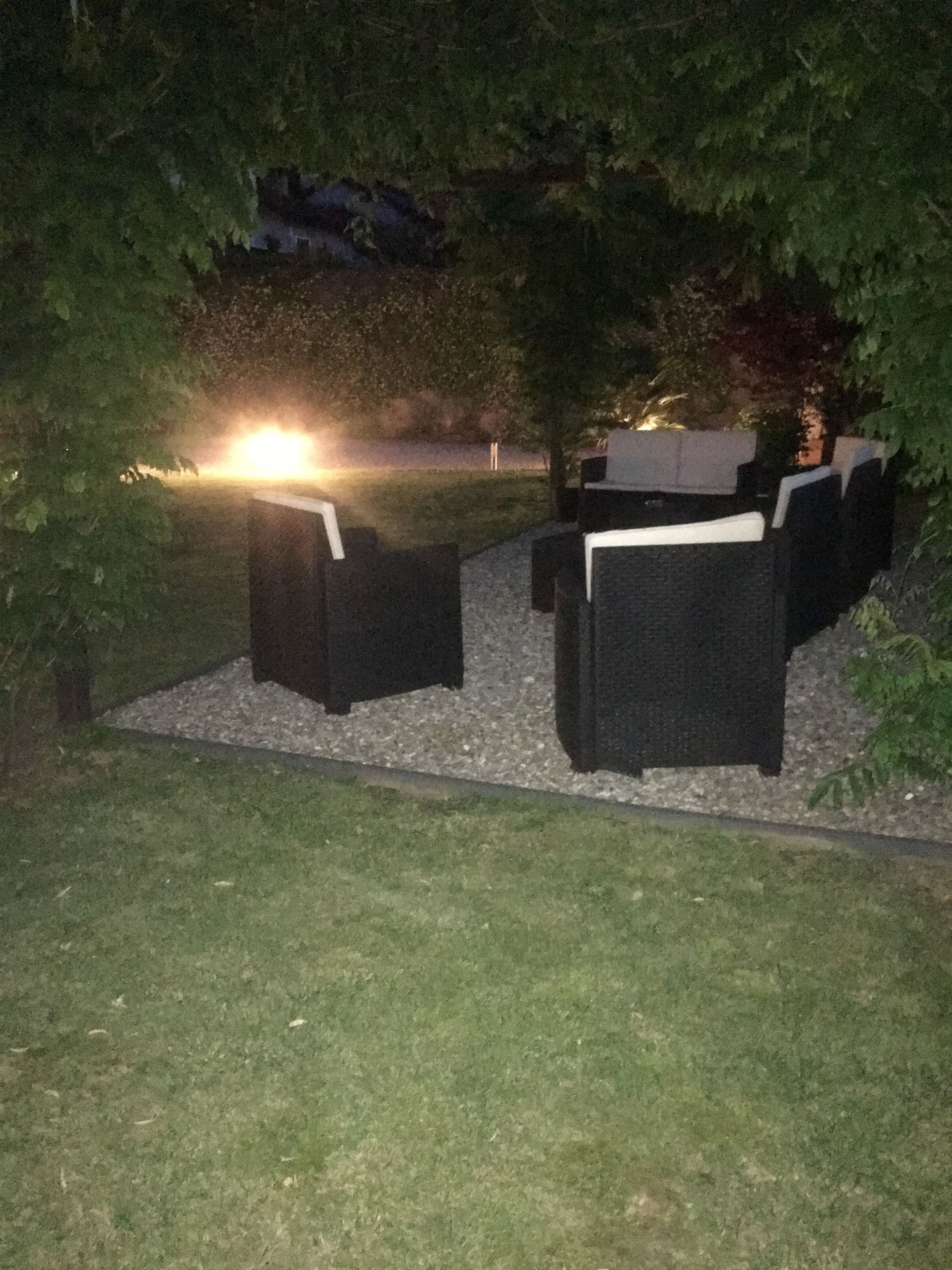 An outdoor seating area with a table and chairs, surrounded by greenery.