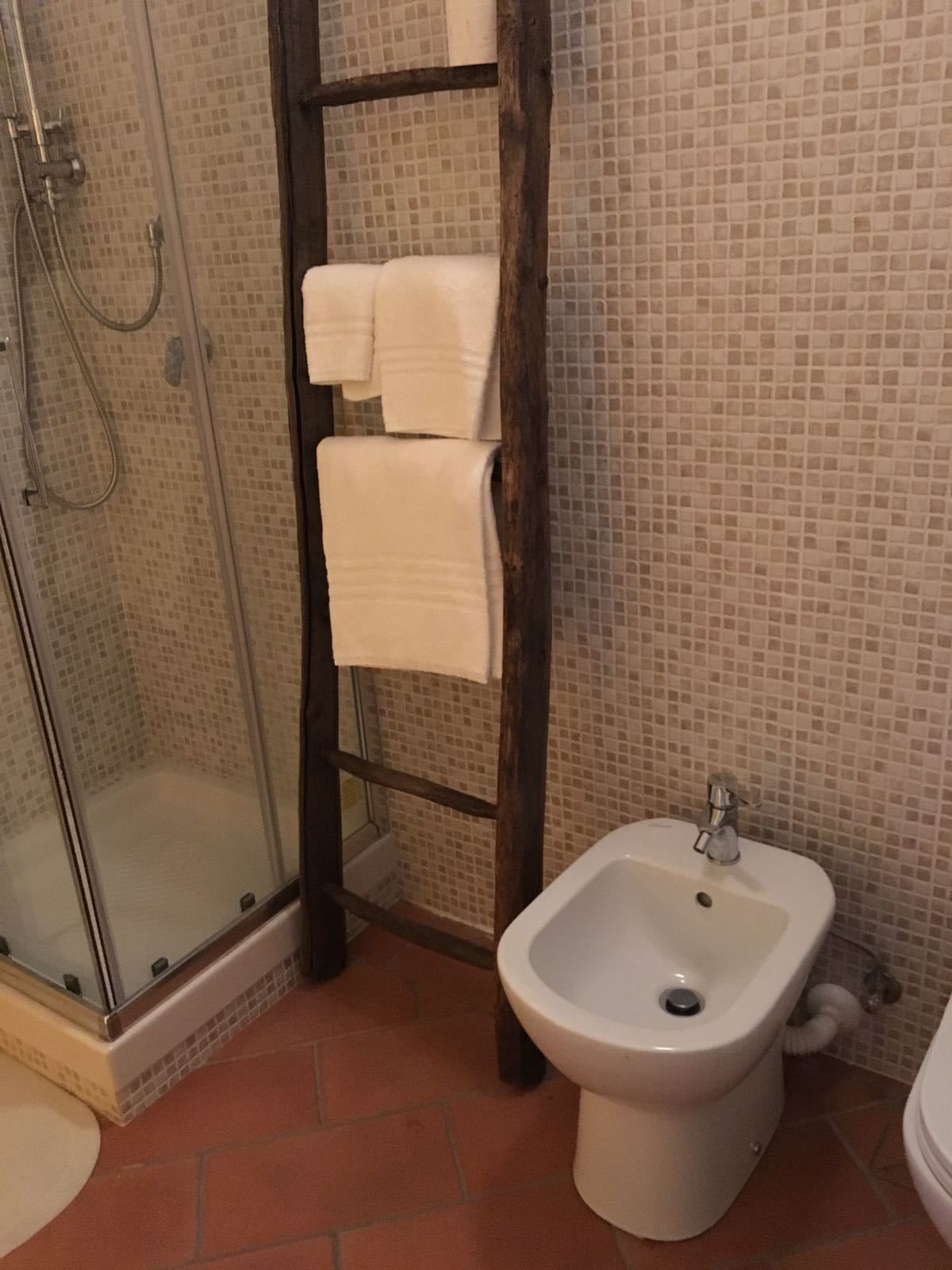 Egy fürdőszoba üveg válaszfallal ellátott zuhanyzóval, bidével és csempézett fallal.