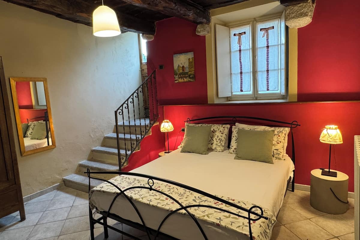 A bedroom with a bed, a window with curtains, a staircase, and a mirror.