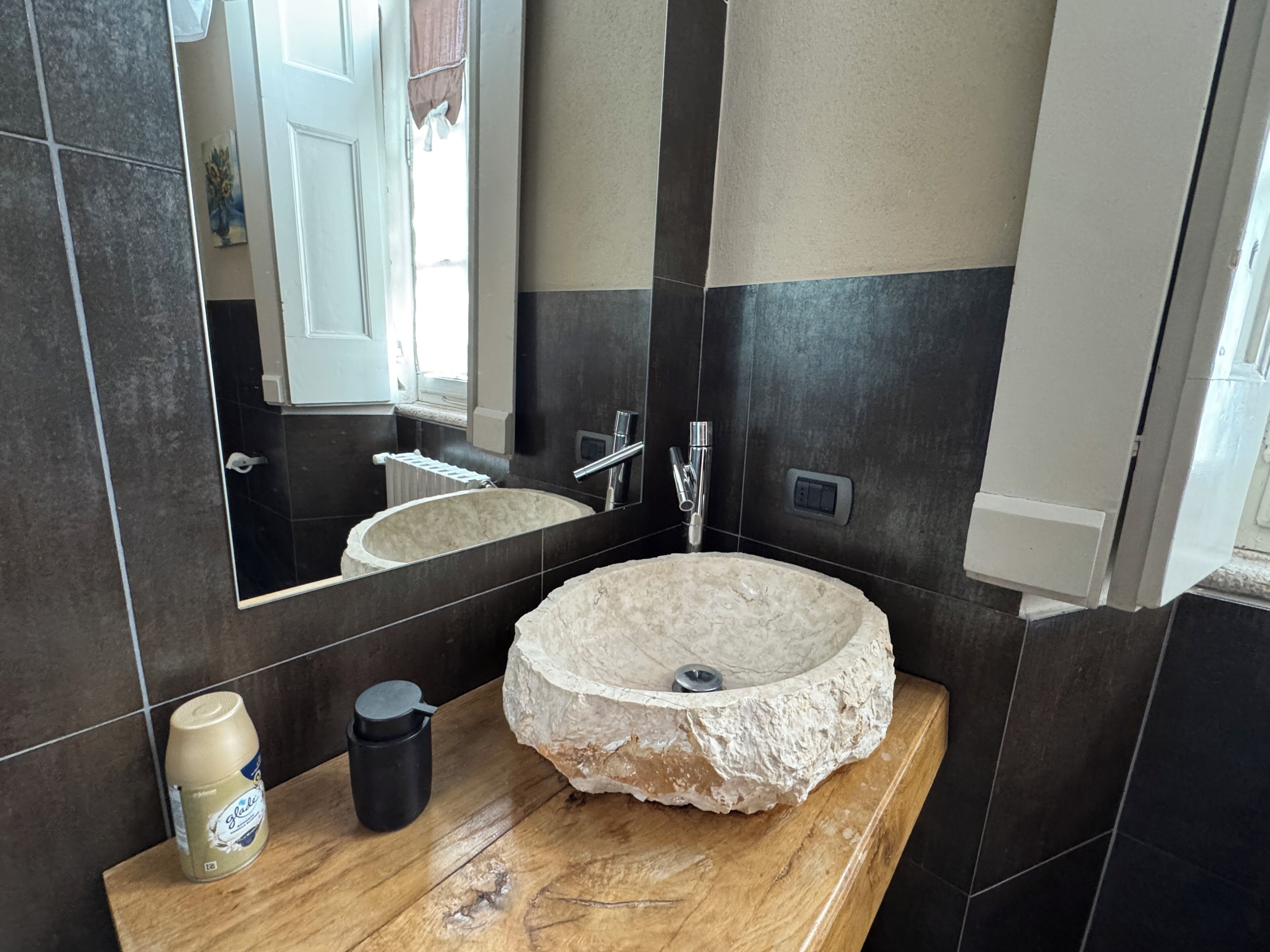 A bathroom with a round stone sink, a mirror, a wooden countertop, and a bottle of hand soap.