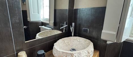 A bathroom with a round stone sink, a mirror, a wooden countertop, and a bottle of hand soap.