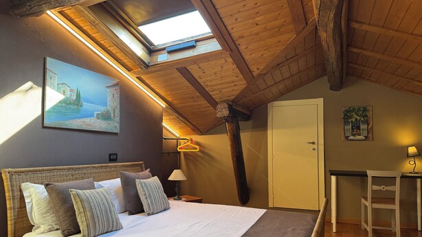 A bedroom with a bed, a desk, a chair, a wardrobe, and a painting on the wall. - II Torchio - Guest House (Dormelletto)