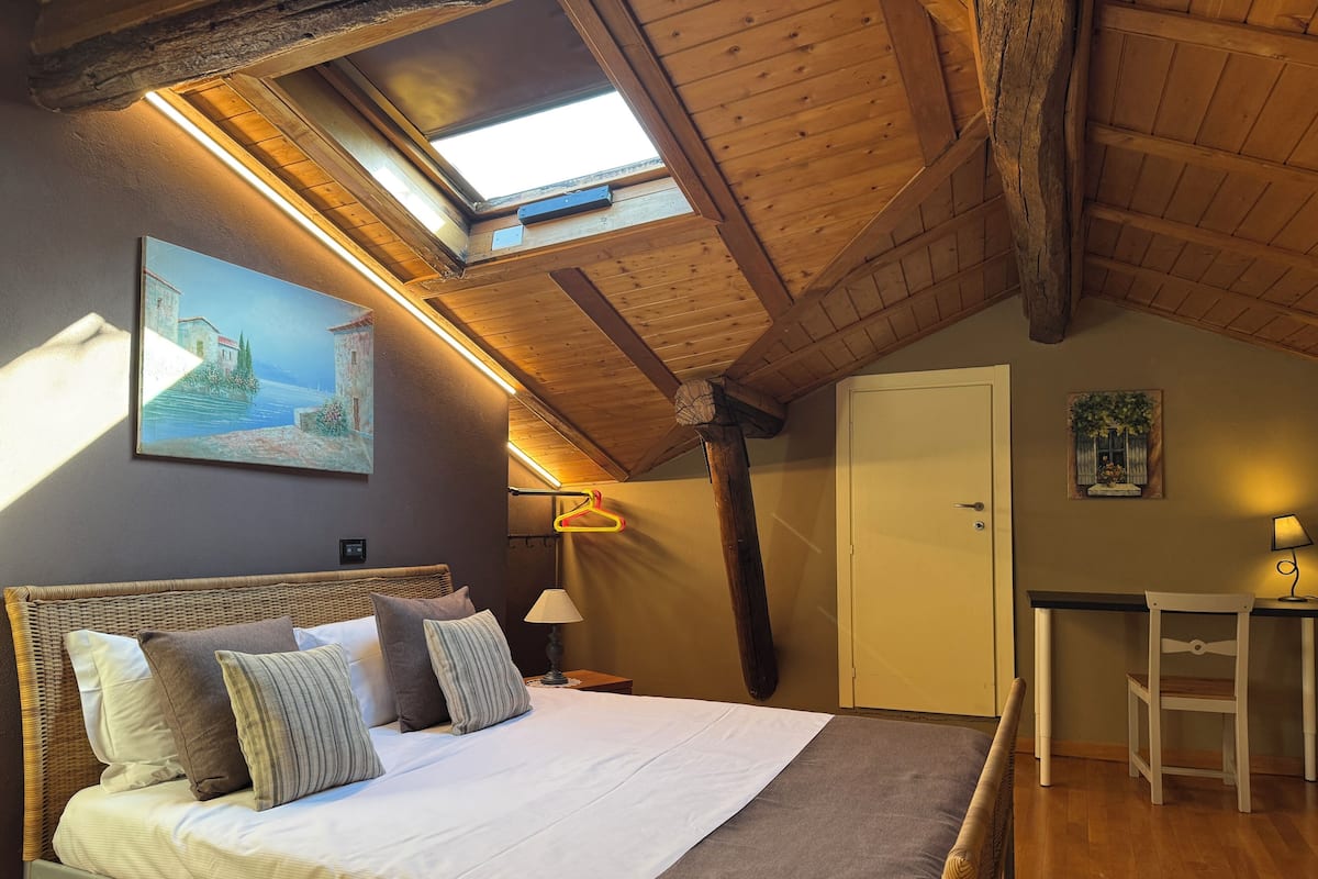 A bedroom with a bed, a desk, a chair, a wardrobe, and a painting on the wall.
