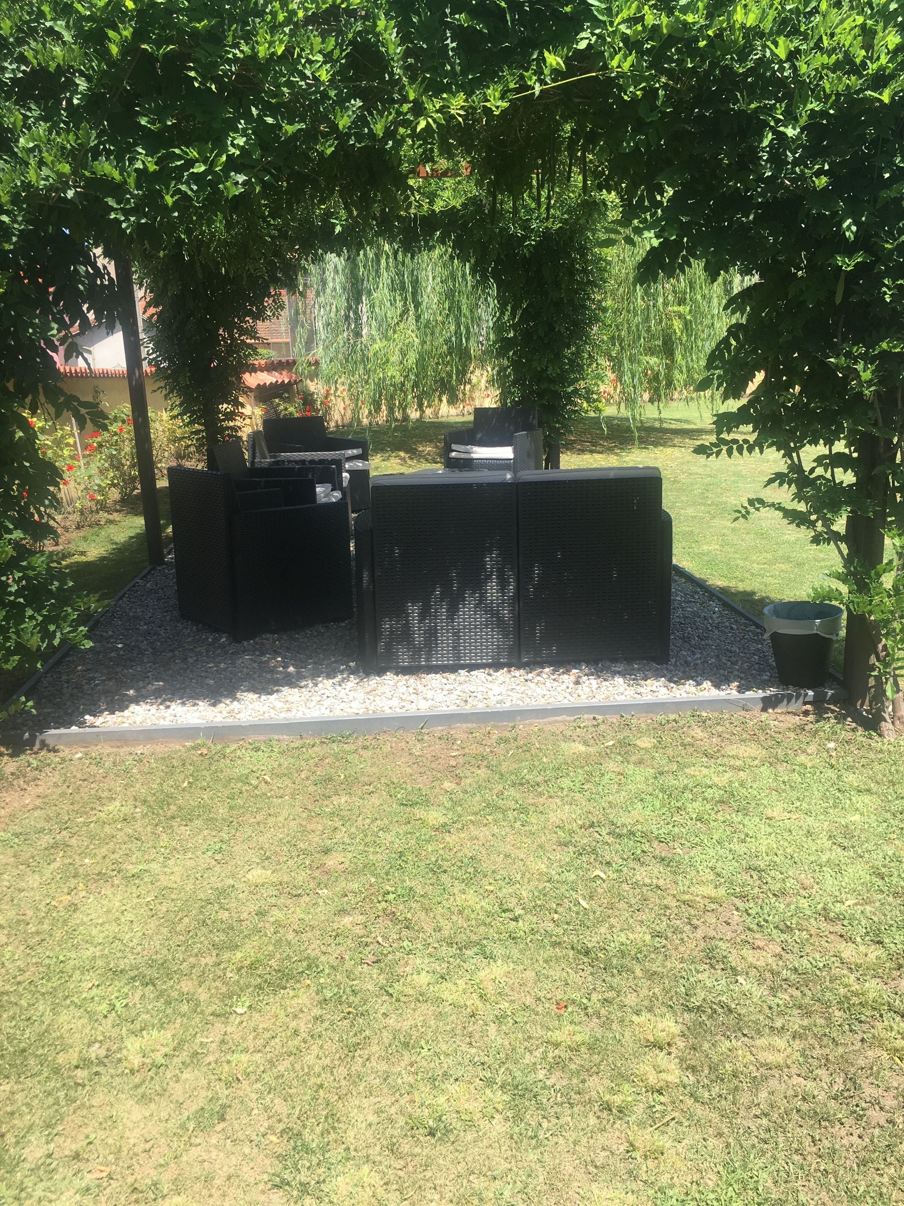 Un espace patio aménagé avec du mobilier d’extérieur, un barbecue et un jardin agrémenté d’arbres et de plantes.