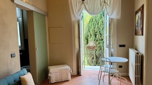 A room with a blue sofa, a small table with chairs, a radiator, and a view of greenery through a window. - II Torchio - Guest House (Dormelletto)